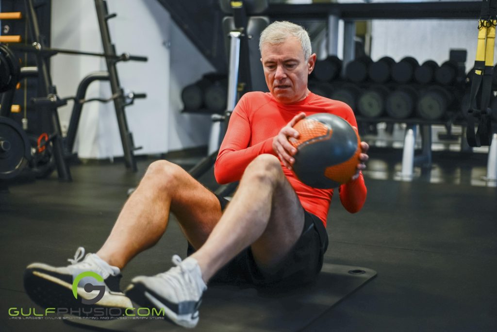 An older man working out at the gym with a medicine ball.