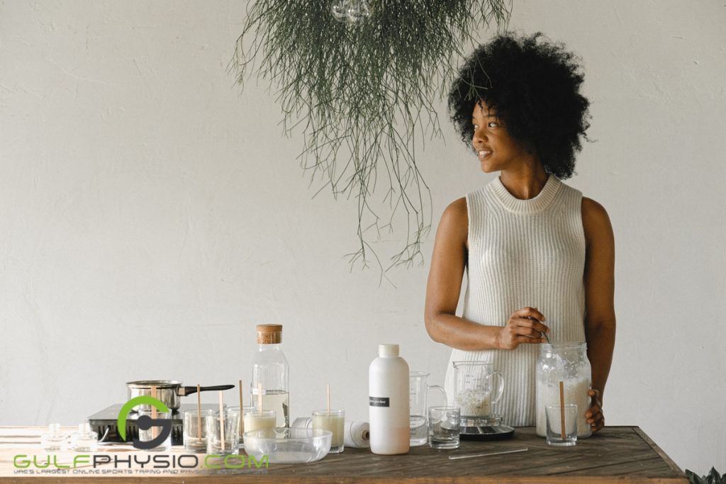 Woman looking sideways while scooping paraffin wax and standing over a table full of ingredients and equipment like a portable stove and the like