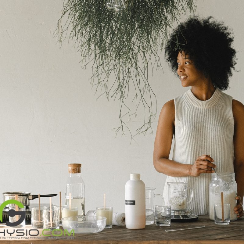 Woman looking sideways while scooping paraffin wax and standing over a table full of ingredients and equipment like a portable stove and the like