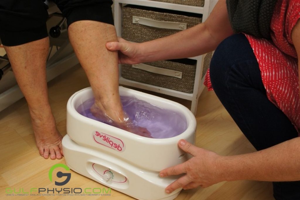 A person is dipping another person's foot in a melted paraffin wax bath