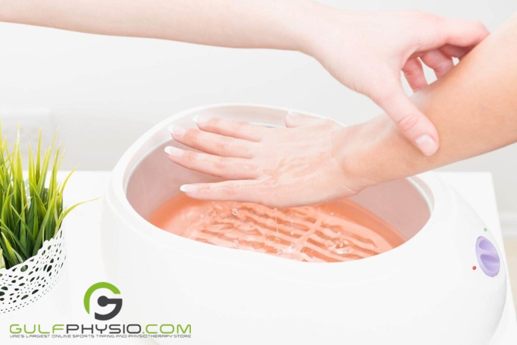 A hand dipping another hand in a warm paraffin wax therapy bath