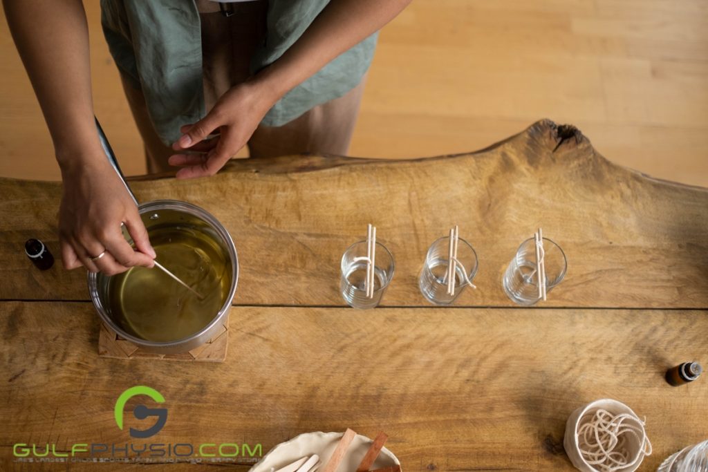 A person is mixing melted paraffin wax and fragrance oils to pour the mixture into the prepared glasses with wicks