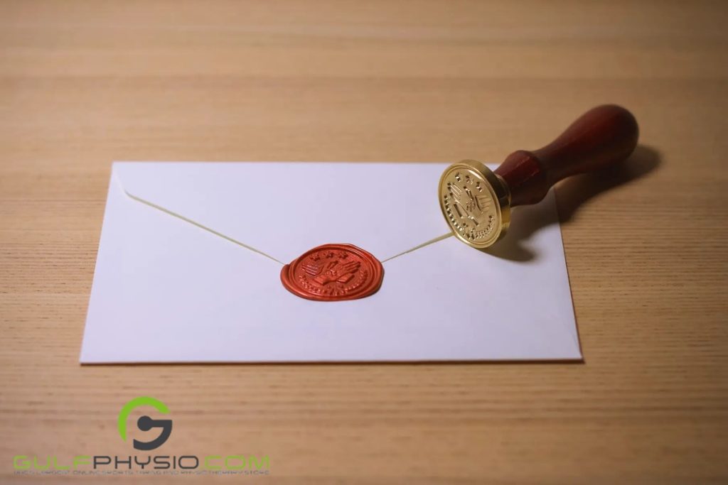 A red wax seal is stamped on a white envelope while the stamp is on its side on the table