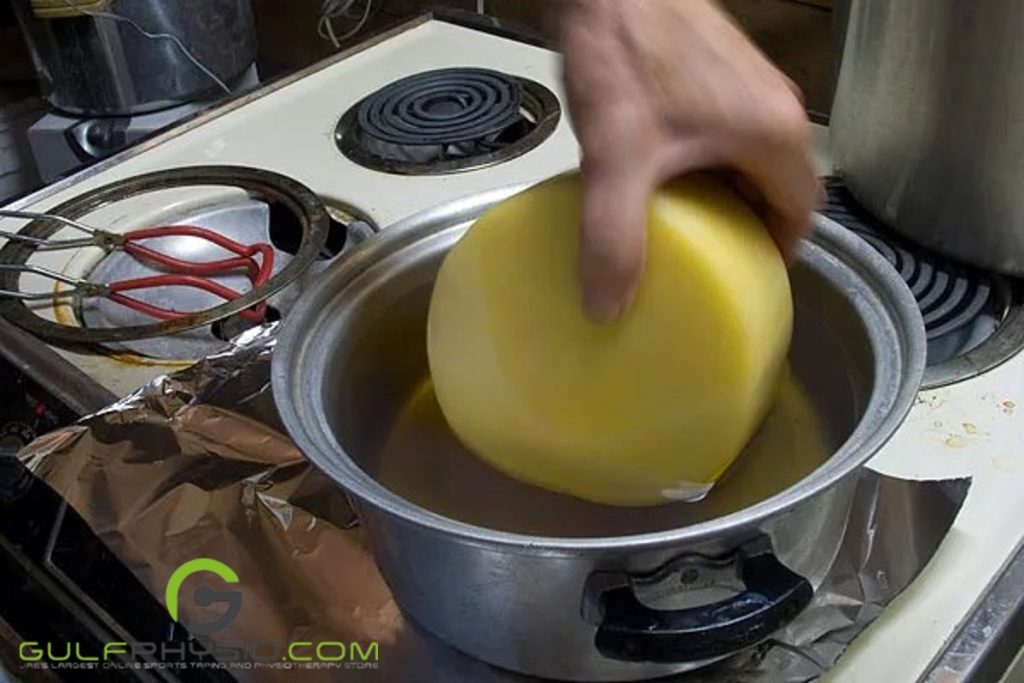 A person is dipping an entire wheel of cheese in a pot of melted paraffin wax