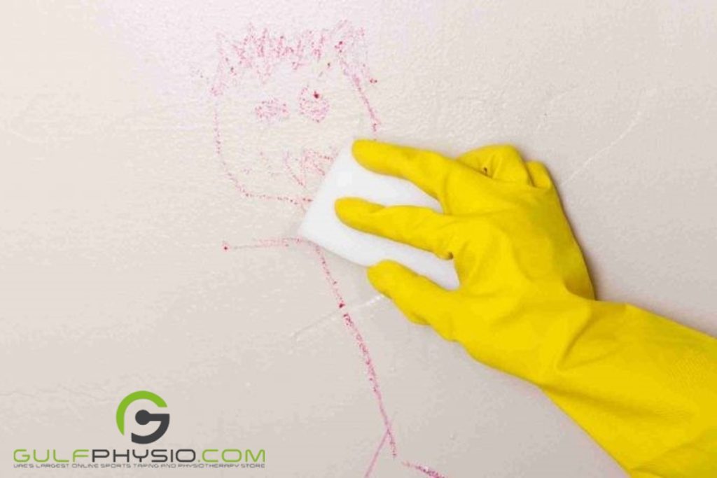 A hand with a yellow glove rubbing paraffin wax on the crayon drawing on a wall