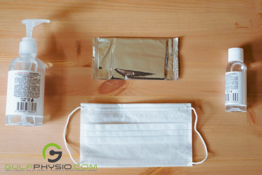 Alcohol-based sanitizers and wipes with a face mask are on a wooden table