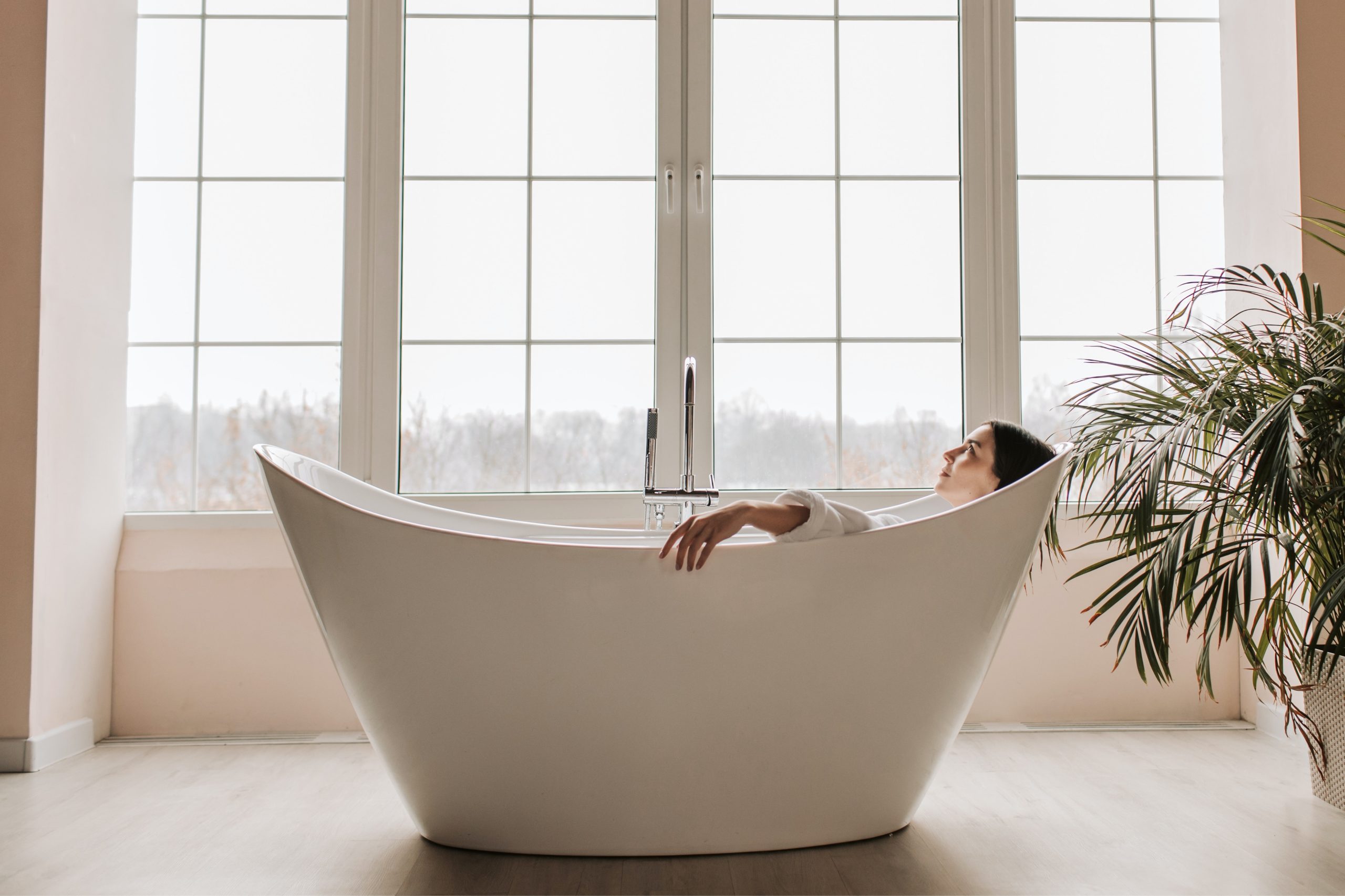 A woman is enjoying her Epsom salt bath in her spacious bathroom with very wide windows