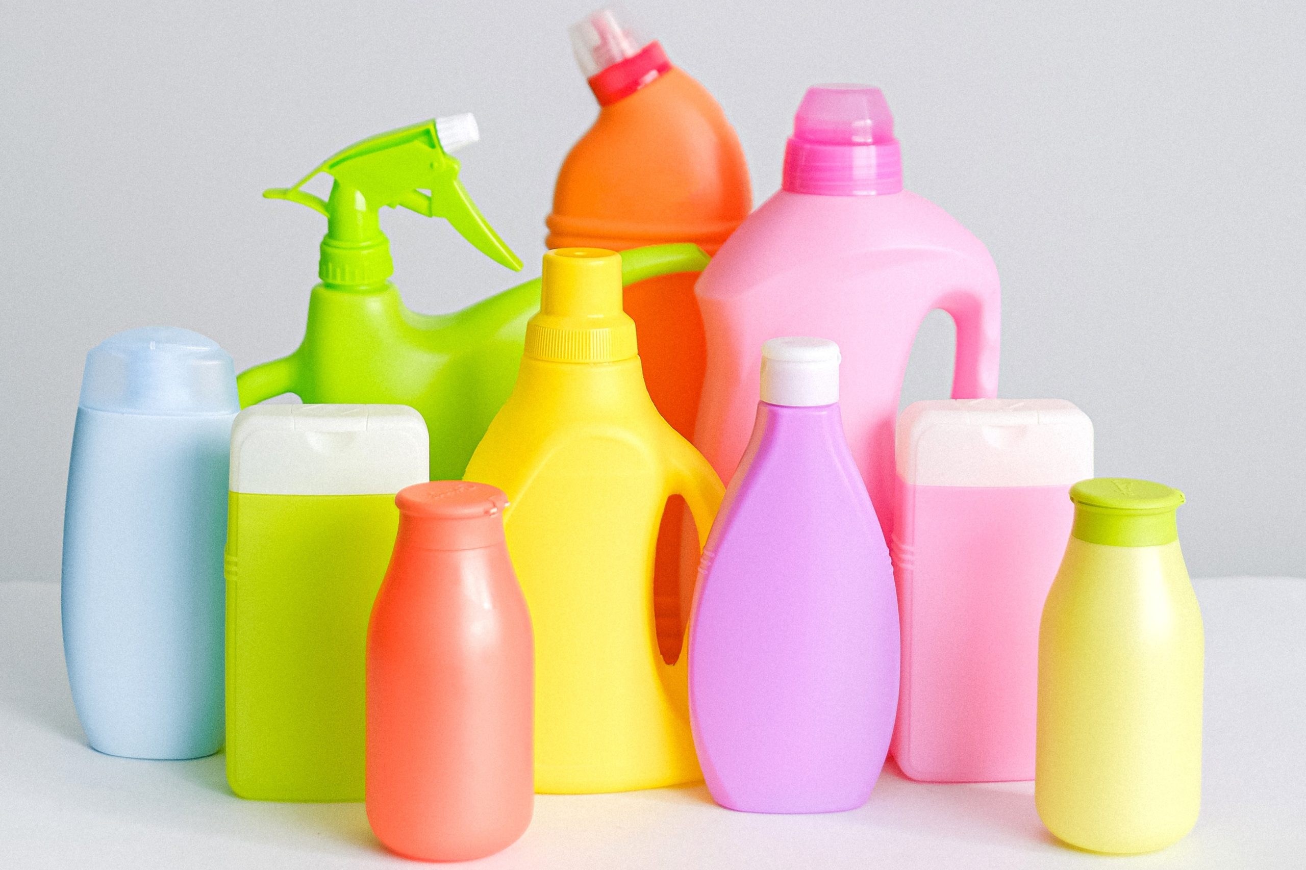 Different-sized and different-coloured bottles of disinfectants and antiseptics are arranged on a white table while in front of a white background