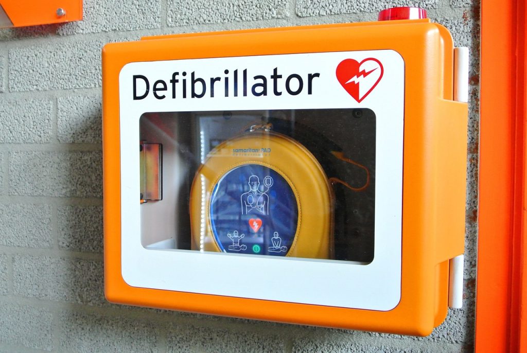 In a yellow box on a grey brick wall for better visibility, an AED is ready 