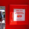 An AED is placed in a red box for emergencies right on a red wall beside a mounted telephone