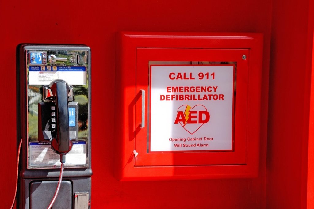 An AED is placed in a red box for emergencies right on a red wall beside a mounted telephone