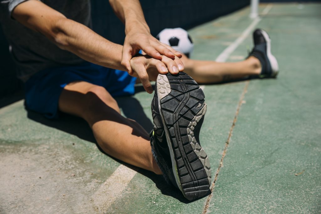 A football player before a game is stretching their ankles