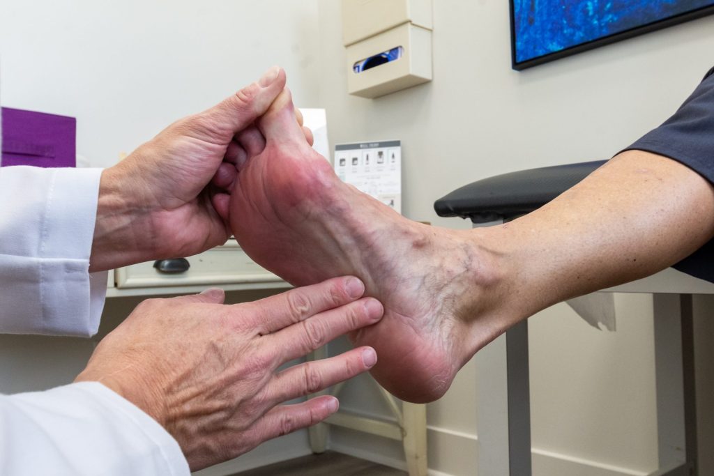 A medical professional like a physiotherapist checking the foot and ankle of a patient for signs of an ankle sprain