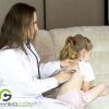 A pediatric doctor conducting a check-up on a young girl. The doctor is listening intently, as her stethoscope is placed on the young patient's back.