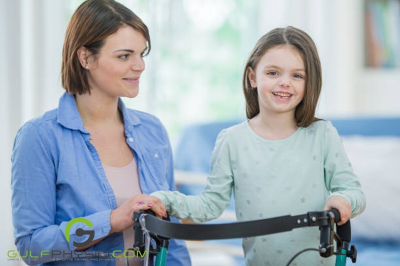 A young girl using an assistive walker smiles for a photo as her mother smiles at her.