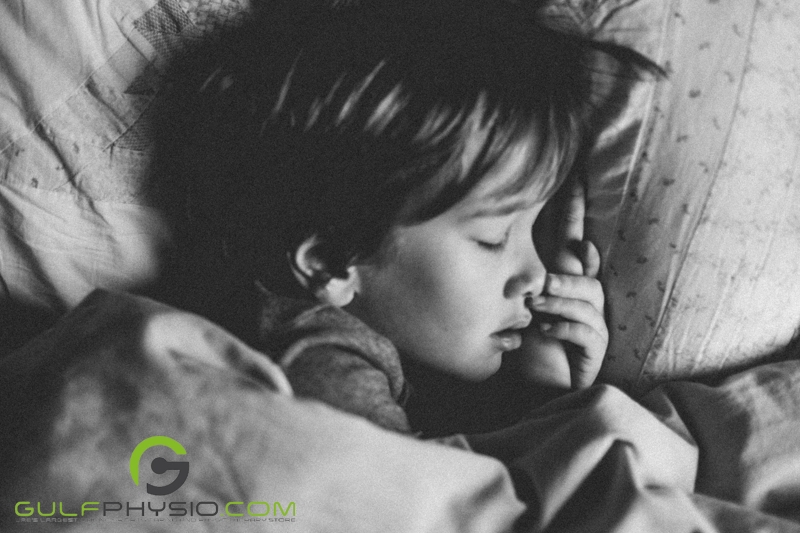 A black and white photo of a young boy asleep in bed.