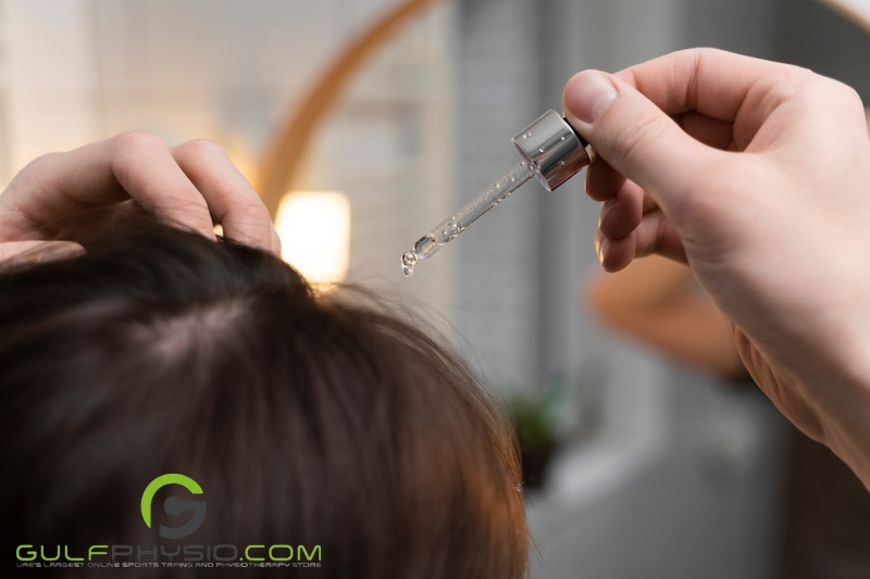 A close-up of the top of a person's head as they apply serum to their scalp using a dropper.