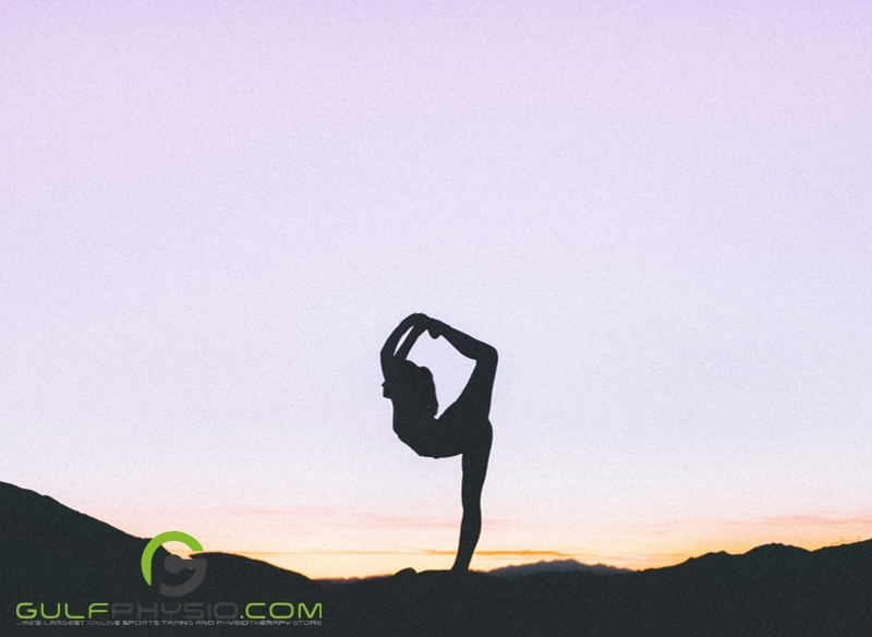 A silhouette of a woman in the middle of a “standing bow” yoga pose.