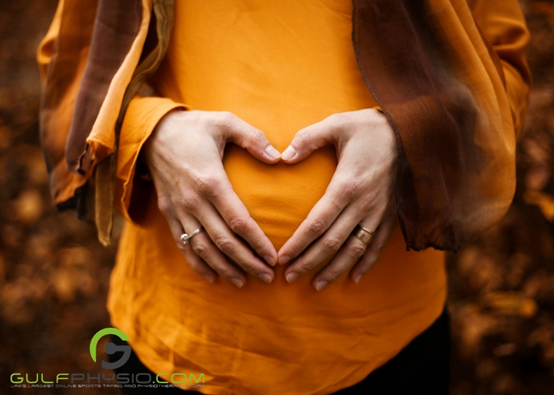 A close-up photo of a pregnant woman’s belly. She is making a heart shape with her hands over her belly.