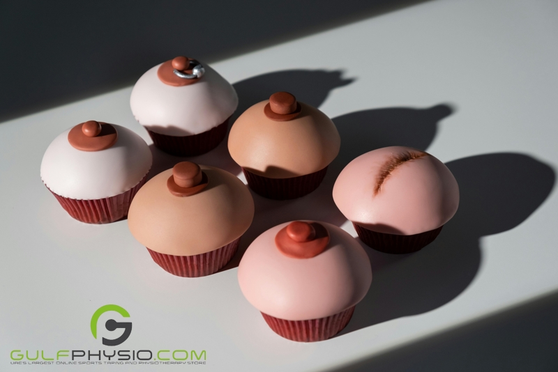 A visual representation of different breasts and the effect of breast cancer using cupcakes that look like breasts. From top left to bottom right: A pair of cupcake breasts with a pierced left nipple, a healthy pair of cupcake breasts, and a pair of cupcake breasts with the left cupcake visualizing what a mastectomy scar looks like. 