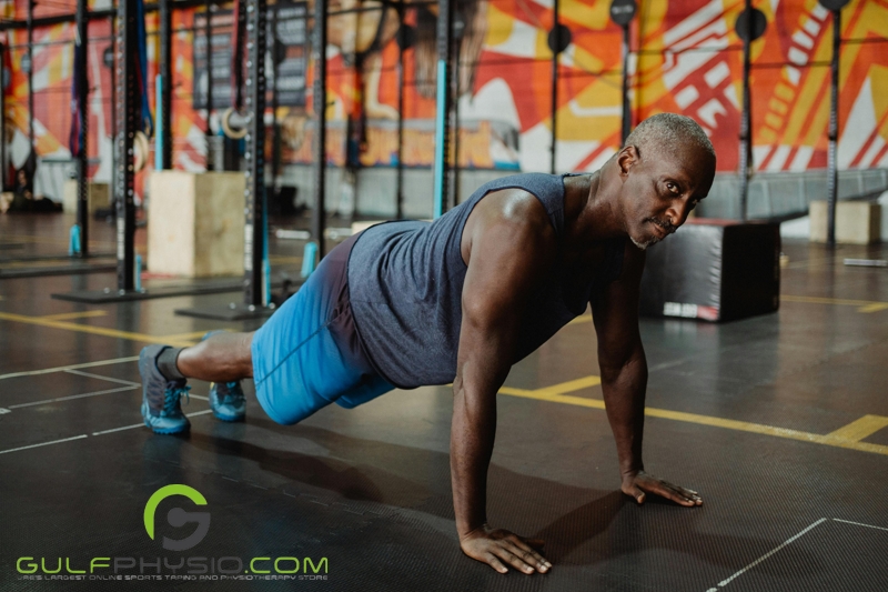  An older gentleman staying fit by doing a full plank at the gym.