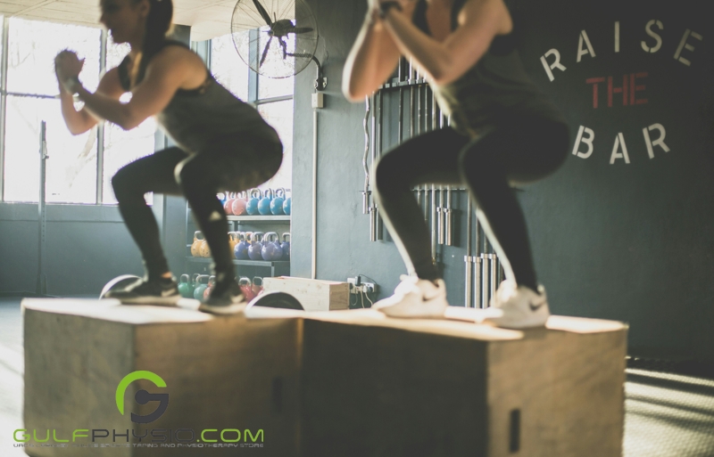 A close-up image of two gym enthusiasts doing box jumps on jump boxes at the gym.