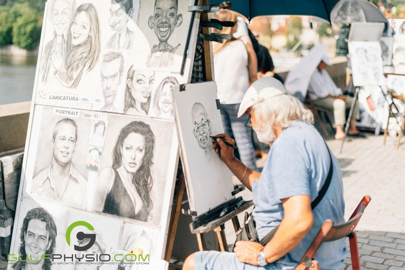 A street artist with glasses and gray hair; drawing highly detailed caricatures of people.