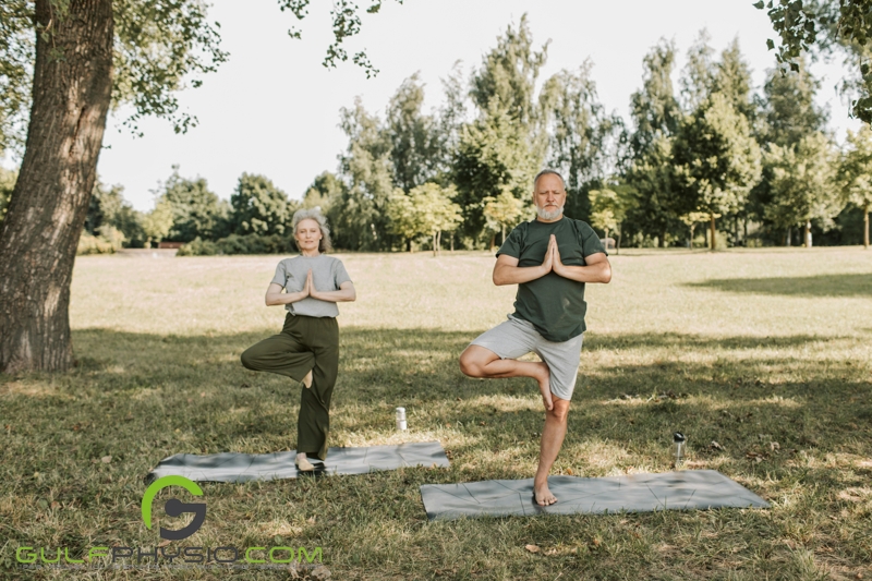 An older man and woman practicing yoga in a park.