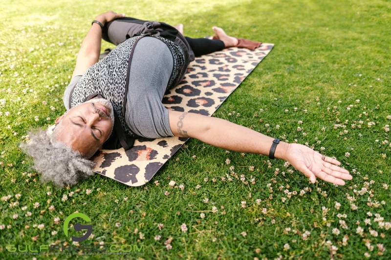 An older gentleman practicing yoga on a grass covered field.