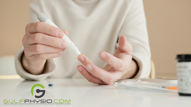  A close-up photo of a woman’s hands as she takes a blood sample using an automatic medical lancet. There is a syringe and a bottle of pills on the table in front of her.