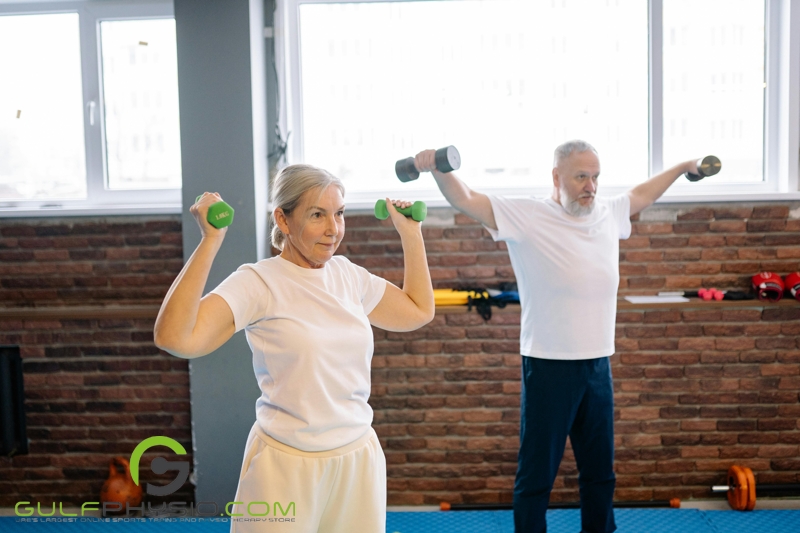 An older man and woman working out with lightweight barbells at the gym. 